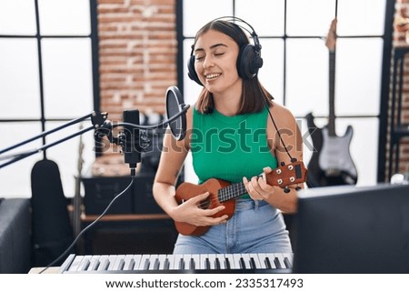 Young hispanic woman musician singing song playing ukelele at music studio Royalty-Free Stock Photo #2335317493