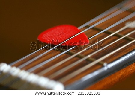 Red guitar pick macro close up. Acoustic guitar. Wooden. Wood. Neck. Strings. Musical instrument. Vintage. Narrow depth of field. Selective focus. Hobby. Entertainment. Play. Song.  Royalty-Free Stock Photo #2335323833