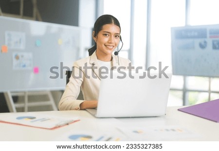 Business young adult asian woman callcenter using laptop computer at office table.
looking at camera smiling with teeth.