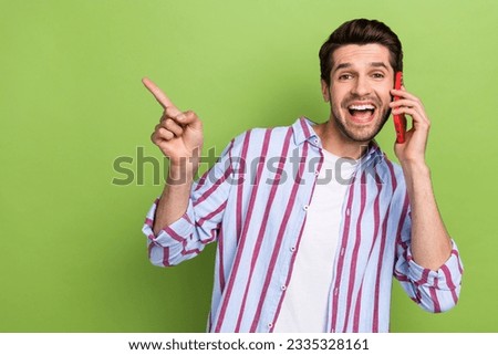 Photo of impressed man dressed striped shirt talking on smartphone indicating at big sale empty space isolated on green color background