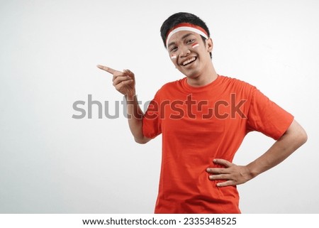 Asian man wearing red and white t-shirt celebrating indonesian independence day with  pointing something gesture on white background.