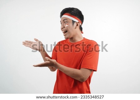 Asian man wearing red and white t-shirt celebrating indonesian independence day with  pointing something gesture on white background.
