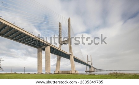 Architectural landmark Vasco da Gama Bridge over the Tagus River in Lisbon, Portugal. Green lawn with trees and cloudy sky. The longest bridge in the European Union.
