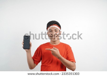 Asian man wearing red and white t-shirt celebrating indonesian independence day with showing blank phone screen on white background.