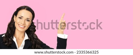 Young happy smiling woman in black confident suit, showing pointing at copy space. Business concept. Rose pink colour background. Brunette businesswoman. Empty area for text.