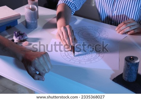 Astrologer showing natal charts to client at table, closeup Royalty-Free Stock Photo #2335368027