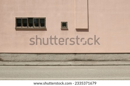 Row of small windows on pink plaster facade. Concrete sidewalk and urban street in front. Background for copy space.