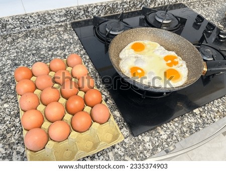 Chicken eggs in a frying pan while frying on stove. Cooking an omelet and scrambled eggs from a chicken egg. Natural organic eggs in cardboard package on table in kitchen. Eggs for breakfast. 
