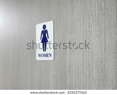 The symbol depicts a woman in blue, set against a sleek silver background, tastefully affixed to a weathered gray wooden door. This unmistakable sign effortlessly identifies the women's restroom, ensu
