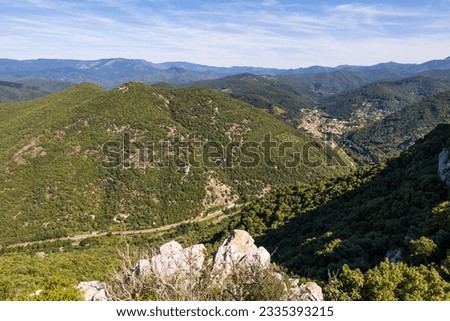 Valley and road leading to the village of Sumene from Ganges, south of the Cevennes, dominated by the cliffs and forest of the Combe Chaude Regional Nature Reserve and the summit of the Ranc de Banes Royalty-Free Stock Photo #2335393215