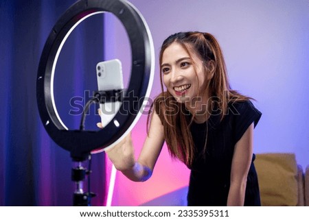 Young trendy influencer asian woman dancing on mobile phone at home in living room with neon light. Creator vlogger talent dancing enjoy hobby content recording show video sharing on social media. Royalty-Free Stock Photo #2335395311