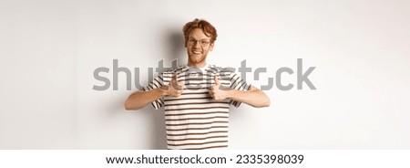 Cheerful redhead guy in nerdy glasses showing thumbs-up, smiling and saying yes, agree or like something, standing over white background.
