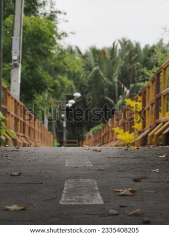 A narrow walk way with yellow orange fences on the sides surrounded with trees and dried leaves on the ground