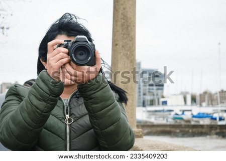 front view of young woman standing on pier by the river using DSLR digital camera creating content for social media.