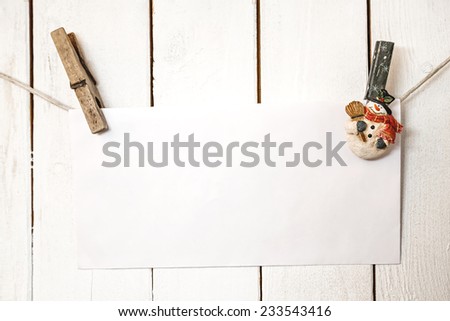 Christmas snowman clothespins hanging on clothesline or rope and holding greeting white blank paper card on wooden background