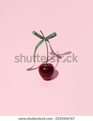 Creative aesthetic fruit concept, juicy cherry with a green satin bow, candy pink background. 