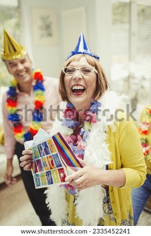 Portrait laughing mature woman in party hat holding birthday gift