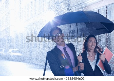 Happy businessman and businesswoman walking under umbrella in rain Royalty-Free Stock Photo #2335454603