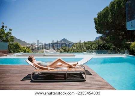Woman sunbathing on lounge chair next to luxury swimming pool mountain view Royalty-Free Stock Photo #2335454803