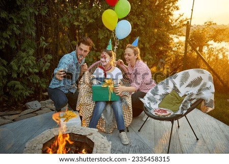 Joyful and festive family of three, celebrating girls birthday, taking a picture outdoors in the backyard by a fireplace. Family, celebration, togetherness concept.