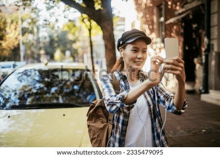 Young asian woman taking a picture with her smart phone while walking on the city street