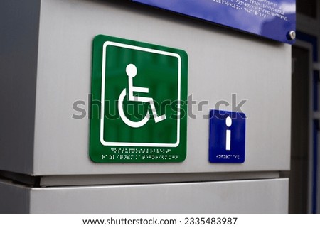 Green logo of a person on a wheelchair with braille text. A sign with information for blind people and people with disabilities in front of the bank entrance