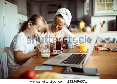 Single mother and daughter having breakfast together in the morning while using a laptop in the kitchen Royalty-Free Stock Photo #2335496571