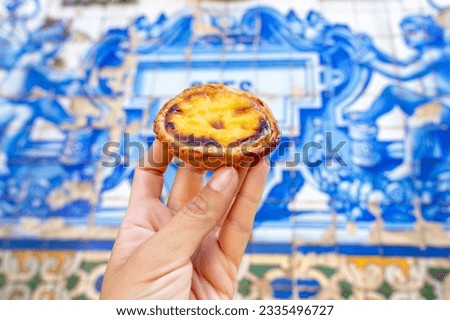 holding Pastel de nata in Porto Portugal in front of beautiful white blue azulejo tiles . Royalty-Free Stock Photo #2335496727