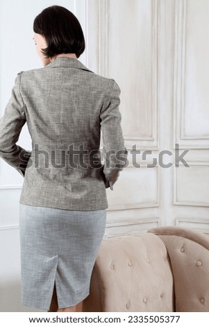 Unrecognizable beautiful woman in a business gray suit standing and posing with backside in the luxury interior