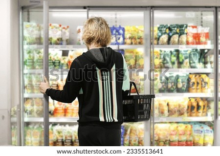  Man choosing frozen food from a supermarket freezer., reading product information Royalty-Free Stock Photo #2335513641
