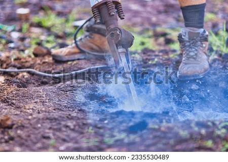 man wearing work boots using a jackhammer that is breaking up rocks and sending dust and debris into the air.   Royalty-Free Stock Photo #2335530489