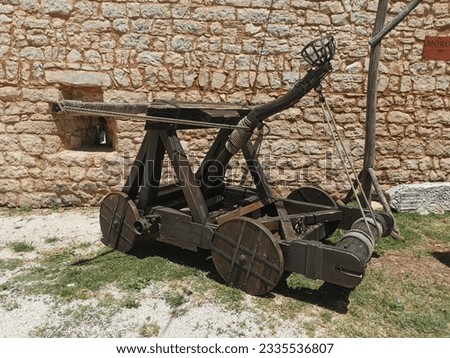 A large  medieval wooden catapult replica by the stone wall on a sunny day
