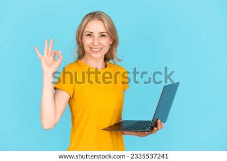 Portrait of cheerful woman holding modern laptop computer, showing ok-sign, standing isolated on blue copy space background. Female smiling, approving good quality of internet connection, web provider