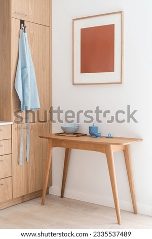 detail in interior at stylish apartment, picture in frame on wall, wooden table with clean plates, ceramic food container and modern cabinet furniture