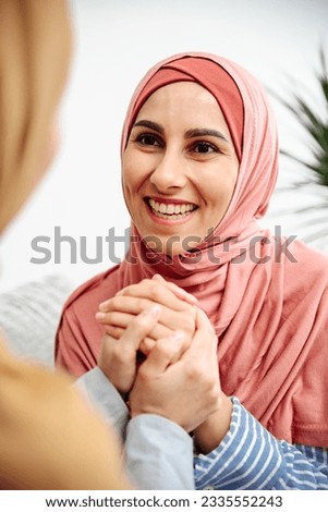 Close up satisfied Muslim woman face enjoy tender moment talking life problems sharing helping with problem, give support apologizing supporting listening sister. Vertical foto. Hands holding hands. Royalty-Free Stock Photo #2335552243