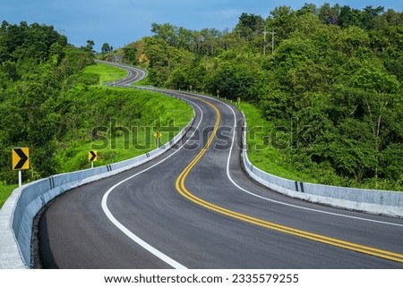 Long curvy forest asphalt road over the hills. Beautiful curved road in the forest. Side view of road. Royalty-Free Stock Photo #2335579255