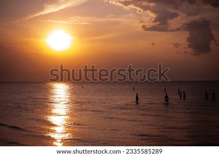 Picture of the sunsetting at a beach with people in the water 