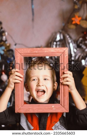 a boy in his hands holds a wooden picture frame close-up against the background of a christmas tree in the room selective focus
