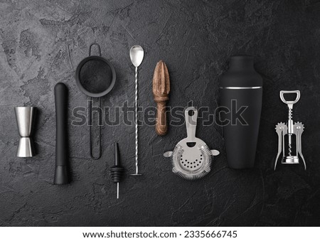 Cocktail utensils black matt steel set on black board background..Shaker,wine opener,spoon,strainer,muddler and jigger with wooden manual juicer. Royalty-Free Stock Photo #2335666745