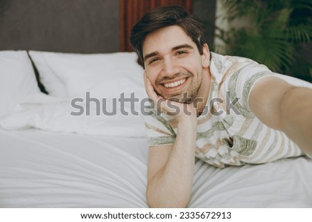 Close up young man wear casual clothes t-shirt pajama lying in bed doing selfie shot pov on mobile cell phone rest relax spend time in bedroom home in own room hotel wake up dream be in good mood day