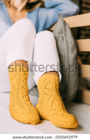 Close up of cozy woman in warm yellow knitted winter socks, white trousers and blue warm sweater resting sitting on a bench at cafe in winter time. Lazy day in knitted socks at cafe. Cozy time. Royalty-Free Stock Photo #2335692979