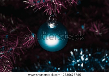 a blue christmas ball close-up. blue christmas ball on a purple tree. blue and pink christmas tree decoration background. turquoise christmas ball