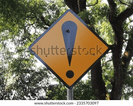 Warning trafic sign pictured with trees and background. Urban photography. Be careful traffic sign. General caution sign.