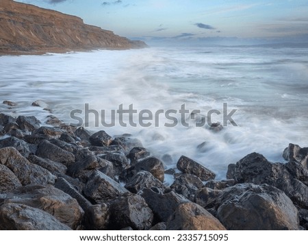 An early morning seascape scene with shiny rocks in the foreground, blurred waves over rocks and high sand stone cliffs going into the distance