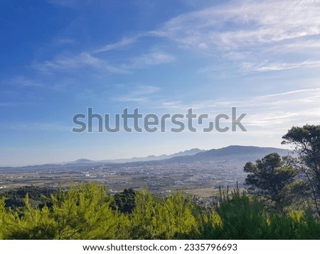City overview from nature. The city is a mixture of old and new buildings, and it is surrounded by mountains. The picture is taken in the daytime, the sun is shining