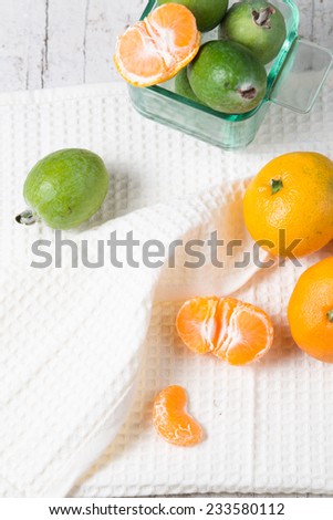 Mandarins and feijoa still life on a white shabby table , with white creamy napkin and pealed tangerines also