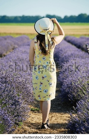 Woman in yellow dress walking in lavender field. Stands her back.