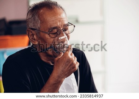 Elderly Senior Man wear oxygen inhaler device for helping breath respiratory. Patient use portable oxygen at home. Patients with respiratory disorders. portable oxygen concentrator or oxygen generator Royalty-Free Stock Photo #2335814937