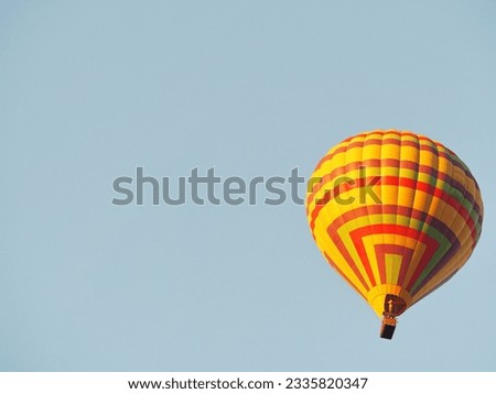 Yellow balloon against the sky in Laos, Vang Vieng. Hot air balloons with passengers flying over blue sky background. The balloons have a reddish yellow pattern. Tourists having fun and taking picture
