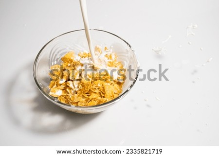 Picture of cornflakes in a glass cup There is milk being poured until Milk splashes out of the cup.